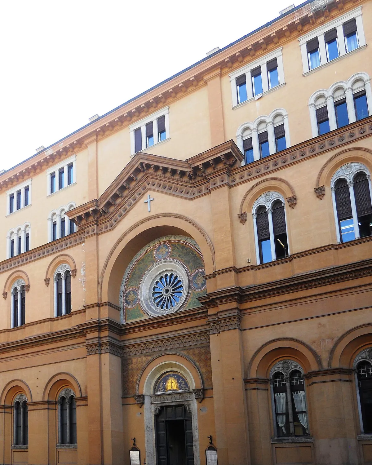 The front of the Waldensian church on Via Quattro Novembre in Rome: a round window in a mosaic arch above a doorway marked Chiesa Valdese, set in an ochre palace front.