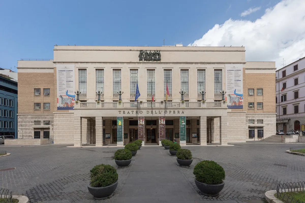 The pale stone front of the Teatro dell'Opera di Roma, with a balcony, tall windows and the name in capital letters over the entrance.