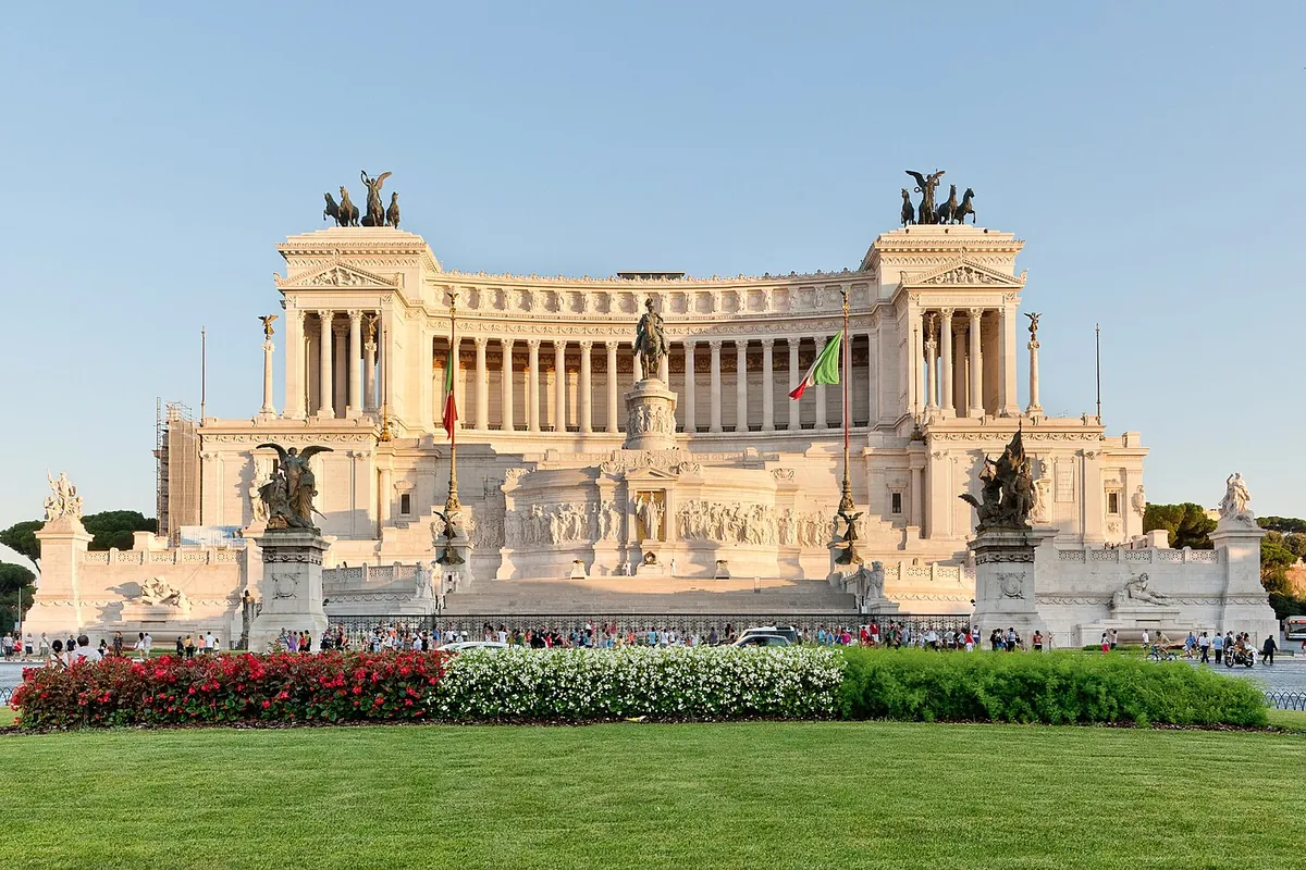 The white marble Vittoriano, the Altare della Patria, on Piazza Venezia in Rome, with bronze chariot groups on the roof and flower beds in front.